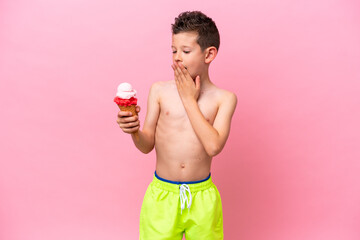 Little caucasian boy eating an ice-cream isolated on pink background with surprise and shocked facial expression