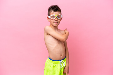 Little caucasian boy wearing a diving goggles isolated on pink background pointing back