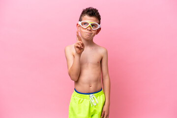 Little caucasian boy wearing a diving goggles isolated on pink background with fingers crossing and wishing the best