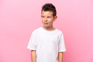 Little caucasian boy isolated on pink background making doubts gesture looking side