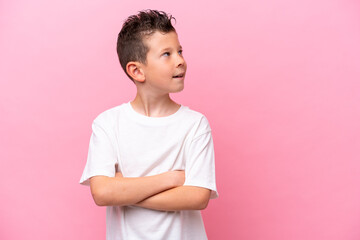 Little caucasian boy isolated on pink background with arms crossed and happy