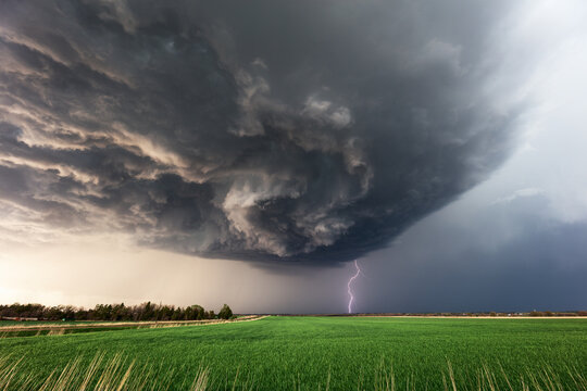 Dramatic supercell storm clouds and lightning strike over a field