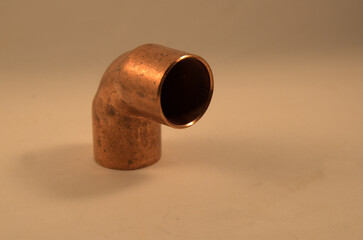 Copper pipe elbow joint on tan background.