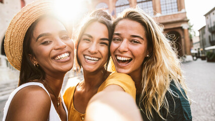 Three young women taking selfie walking on city street - Multiracial females picture smiling at...