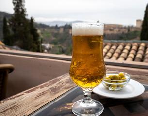 Spanish beer and glass bowl with green andalusian olives served on outdoor terrace with view on Sierra Nevada mountains in Granada, Andalusia, Spain