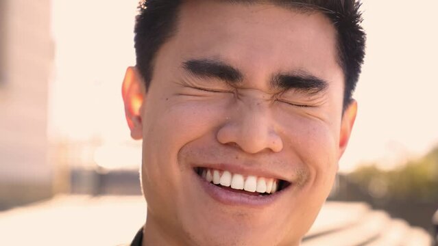 Outdoor portrait of a smiling Chinese guy looking at the camera laughing with positive face and friendly look. Close up of a Happy human face - Cheerful Asian young man. People and emotions.