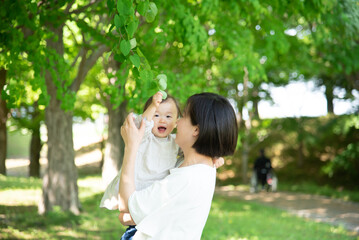 新緑の葉っぱを触る母親と1歳の女の子