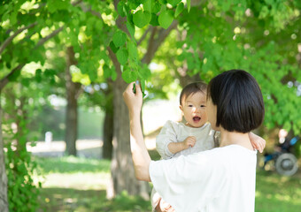 新緑の葉っぱを触る母親と1歳の女の子