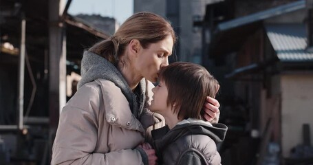 Close up portrait of Caucasian upset mother talking to little son standing outdoors. Mom kissing kid boy in forehead standing on street, refugees flee from war aggression, invasion, conflict, family