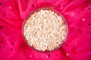 Raw oatmeal flakes on pink background with copy space, porridge as healthy food concept