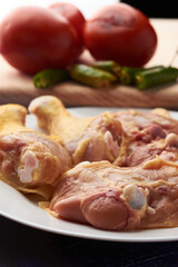 Chicken pieces placed on a plate, garnish tomatoes and chili peppers placed on a wood.