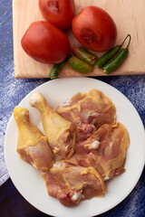 Chicken pieces placed on a plate, garnish tomatoes and chili peppers placed on a wood.