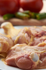 Chicken pieces placed on a plate, garnish tomatoes and chili peppers placed on a wood.