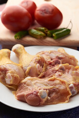 Chicken pieces placed on a plate, garnish tomatoes and chili peppers placed on a wood.
