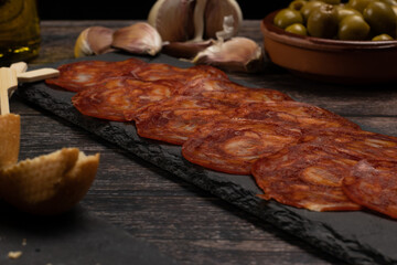 close-up of a plate of Iberian chorizo sausage, sausage on a slate stone plate, on a wooden table with olives, garlic, olive oil and bread. 