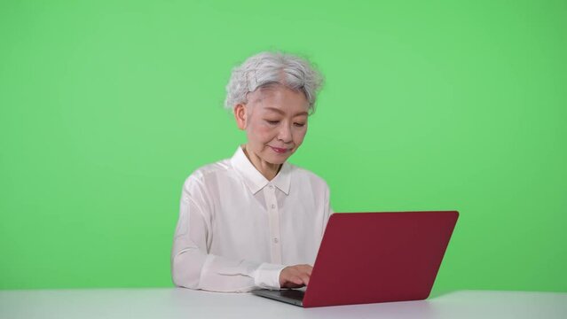 ノートパソコンを使うシニア女性　クロマキー合成用グリーンバック
