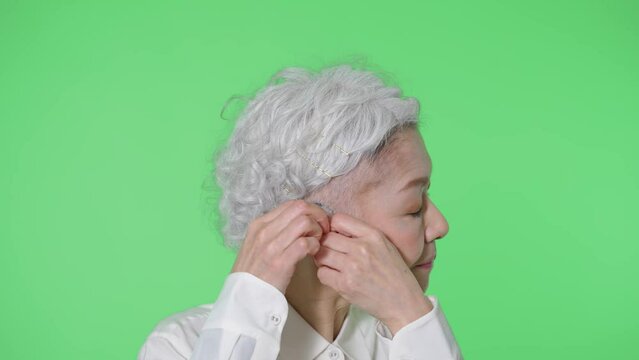 補聴器をつけるシニア女性　クロマキー合成用グリーンバック