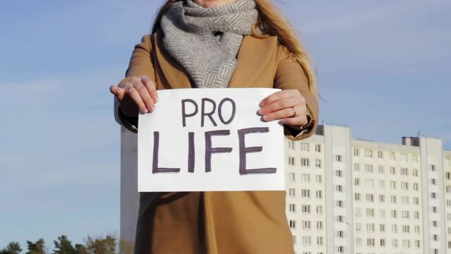 Attractive woman holding paper with PRO LIFE words with cityscape in background. Activism concept