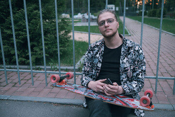 Young irish skater man smiling happy sitting on the bench at the park. © Eugene