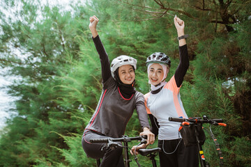 two veiled girls smiling with fists clenched while cycling together in the morning