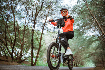 Fototapeta premium bottom view of asian woman in sunglasses cycling on the road with trees in the background