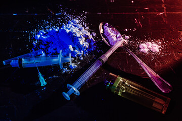 Syringes, spoon, drugs on a black, dimly lit surface. High view. Concept of illegal substances,...