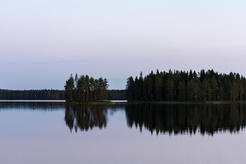 Calm lake in the summer evening in Finland with islands and trees reflecting from the water.