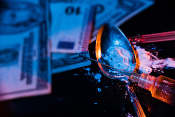 Syringe with cooked Heroin, white powder in a spoon and banknotes on a dark table with two-coloured...