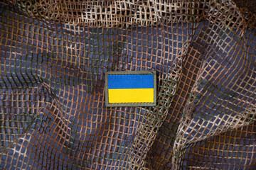 The flag of Ukraine with a stripe on the military uniform of a Ukrainian soldier hangs on a military camouflage mesh,military background,war in Ukraine