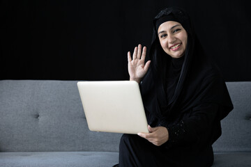 muslim woman using laptop computer, video call to someone on sofa and black background