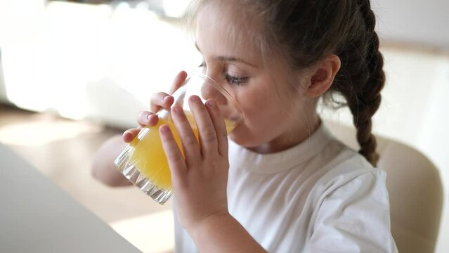 girl child drinking juice. happy family a healthy eating kid dream concept. daughter girl drinking yellow juice from a glass cup in the kitchen. child drinking indoor fruit juice