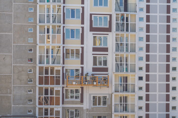 Workers in a suspended cradle paint the walls of a multi-storey panel house with paint