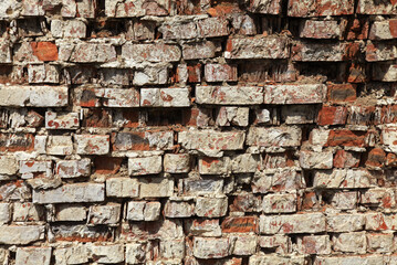 Old brick wall texture. The wall, made of old red bricks, darkened by old age. Ancient vintage brick wall background. Brick wall backdrop. Crumbling and chipped brickwork with traces of whitewash