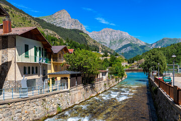 Fototapeta na wymiar Small town and alpine river under blue sky in Piedmont, Italy.