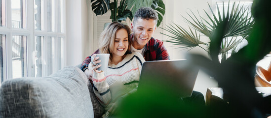 Couple in love at home. Young family watching TV series using laptop and sitting on the couch