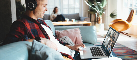 Happy couple domestic life situation. Man watching movie on laptop with headphones and siting on couch and woman at background