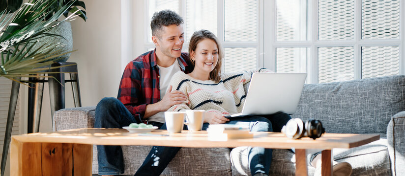 Happy Couple Domestic Life Situation. Man And Woman Sitting Together On A Couch And Watching Movie On Laptop