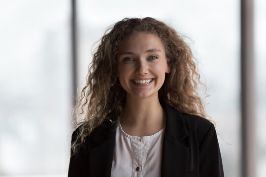 Happy young intern girl looking at camera, smiling, getting job, celebrating career success. Millennial curly hared student woman, office employee, worker, businesswoman head shot business portrait