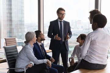 Positive confident business team leader motivating diverse employees at meeting, talking to...