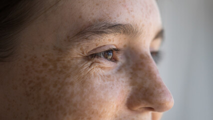 Cheerful freckled young woman looking away, smiling, laughing. Close up of upper face. Cropped shot...