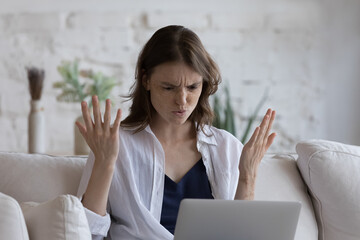 Frustrated angry laptop user woman annoyed with software problem, error, wrong application work, reading letter with concerning news, using computer at home. Modern technology concept