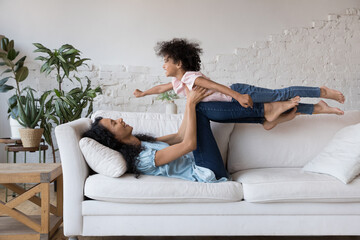 Cheerful strong Black mother exercising with daughter child, holding kid in arms, playing superhero...