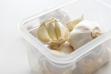 Fototapeta na wymiar Garlic cloves and bulbs in a plastic box container. Photo can be used for the concept of how to keep garlic fresh longer.