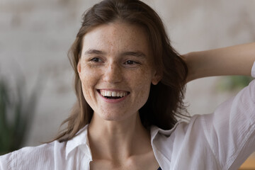 Joyful excited model girl with spotted facial skin indoor portrait. Freckled young woman with natural makeup, white teeth posing indoors, looking away, laughing, dreaming, smiling. Beauty care concept