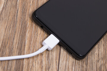 Black smartphone and connected white cable of charger. Telephone charging