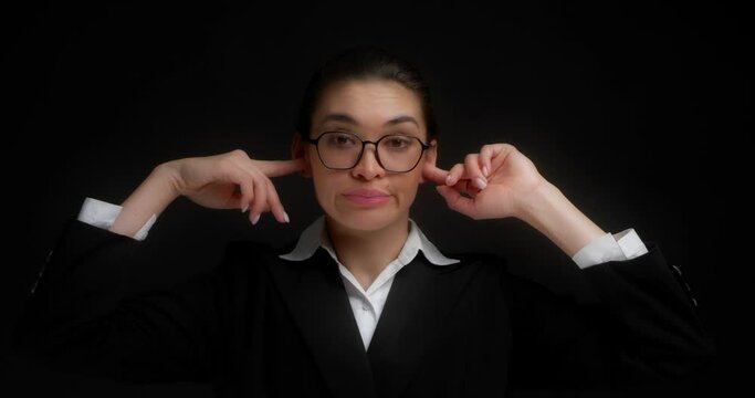 Businesswoman in glasses and office clothes does not want to listen to the interlocutor, plugs ears and says blah, blah, blah.An attractive Asian woman doesn't want to hear anything.Black background.