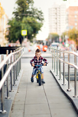 Stylish cute european boy on balance bike in the city, child rides a balance bike on ramp. Summer in the city, comfortable safety urban environment