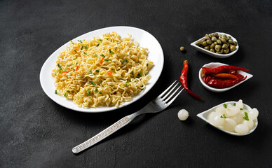 Instant noodles in a white plate on a black background - top view. National fast food. Quick lunch