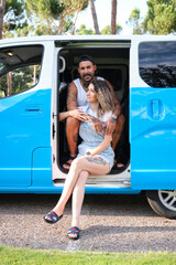 Young tattooed couple smiling and hugging sitting in the side of the van.