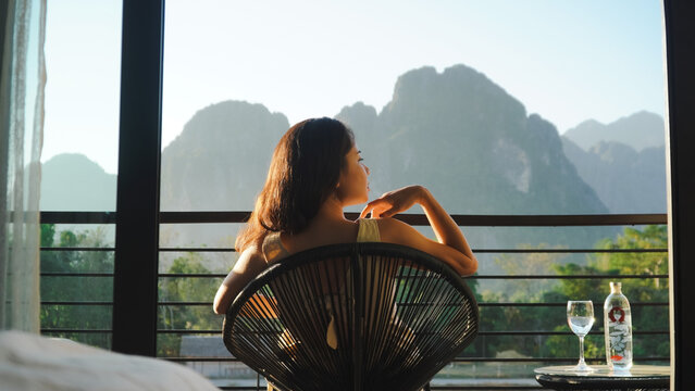 Young Asian woman sitting on the chair with nice scenic mountains background in Vang Vieng, Laos. Vacation concepts.
